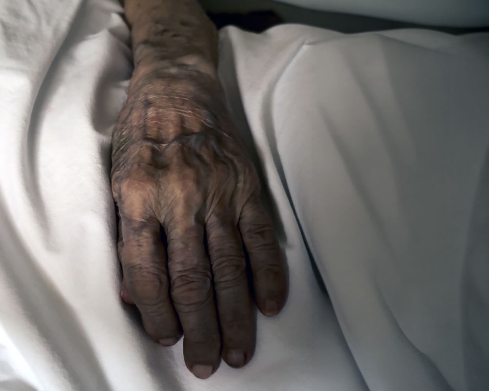 An elderly hand resting on white sheets